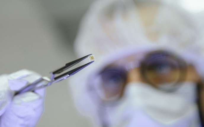 Close-up of a scientist using tweezers to hold a tiny glass-encapsulated device.