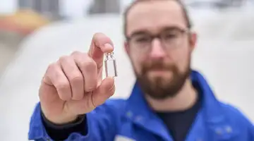 Marius Amschler stands in front of the SCHOTT cullet warehouse and holds a vial up to the camera	