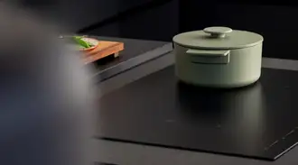 Modern kitchen with black cooking island, matt SCHOTT CERAN® induction cooking surface, green pot and a hand touching the touch control panel.