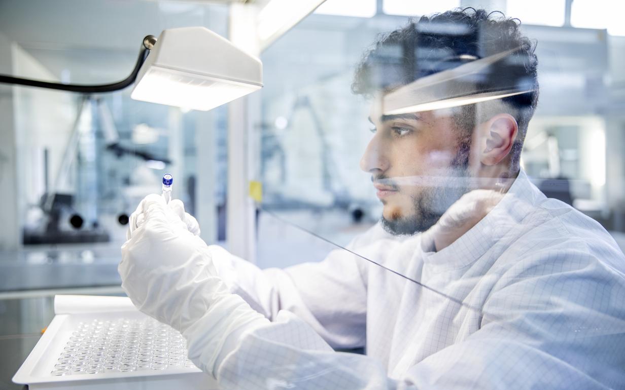 Ein Mitarbeiter in weißem Kittel mit weißen Handschuhen bei der Qualitätsprüfung im Labor.