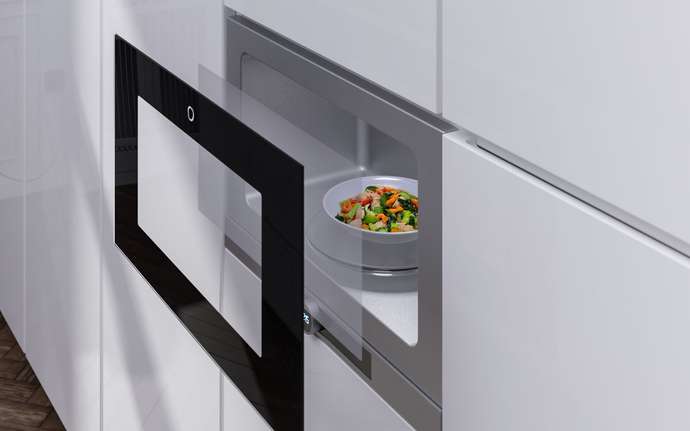 Built-in microwave oven with a clear glass and a bowl of mixed vegetables inside, integrated into a white kitchen cabinet.