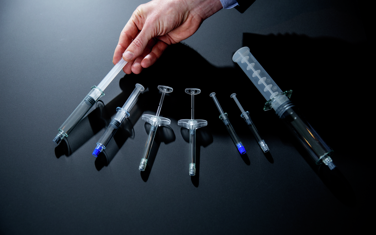 Seven different prefillable polymer syringes on a dark background.