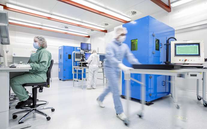 Gowned workers in a cleanroom are pushing a table and working at computers.