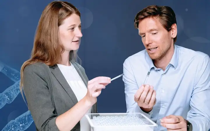 Man and woman discuss pharmaceutical vials behind illustration of molecular structure of glass