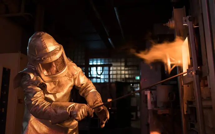 Man in protective suit in front of glass melting tank