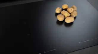 Black matt SCHOTT CERAN® induction hob with raw potatoes and earth crumbs on it.