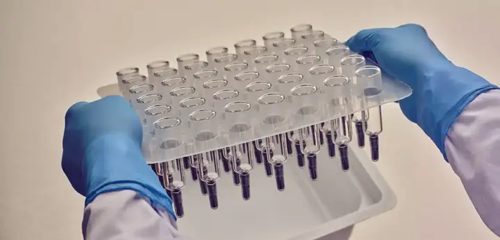 Gloved hands lifting a tray of syringes from sterile packaging in a laboratory setting