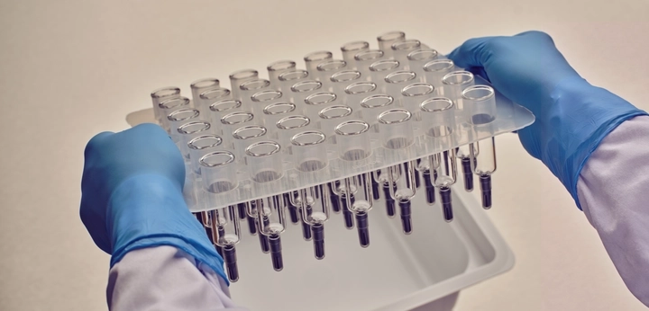 Gloved hands lifting a tray of syringes from sterile packaging in a laboratory setting