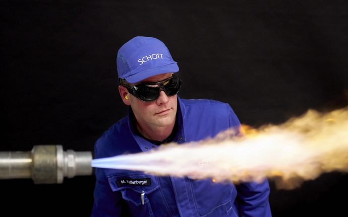 Man in blue SCHOTT work clothes behind a burner.