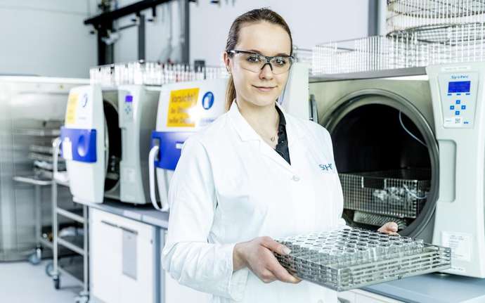 Woman in the laboratory wearing safety goggles and a white lab coat holding a nest of pharmaceutical vials.