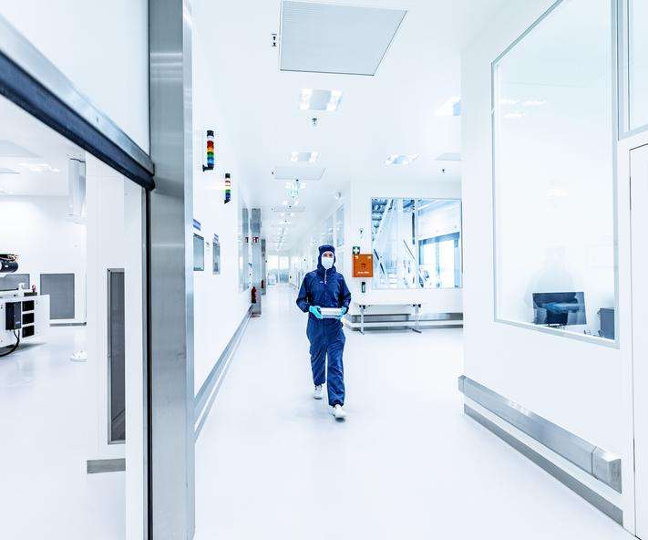 A technician in a cleanroom suit walks through a sterile laboratory