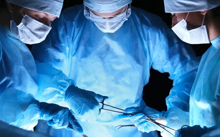 Three surgeons handling medical equipment in a hospital operating theatre