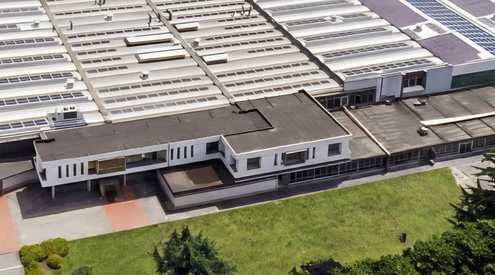 Aerial view of a large industrial manufacturing facility with multiple roof sections covered in skylights and solar panels, surrounded by greenery.