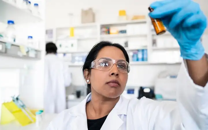 A scientist holds a container between her thumb and index finger.