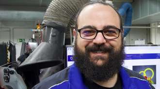 Man with a full beard and glasses in a blue production jacket smiles