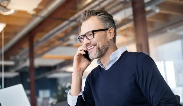 Man in glasses in business office on phone while working on laptop_605x350.jpg