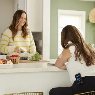 A woman wearing an iLet Bionic Pancreas on her hip eats lunch with a friend.