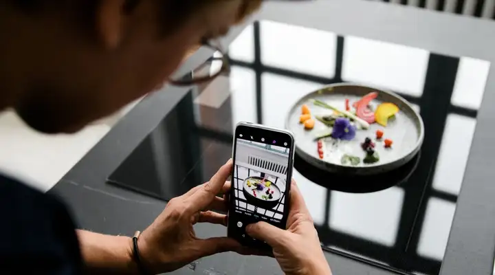 Someone takes a picture using a smartphone of a bowl with a creative vegetable arrangement on a vitroceramic cooktop