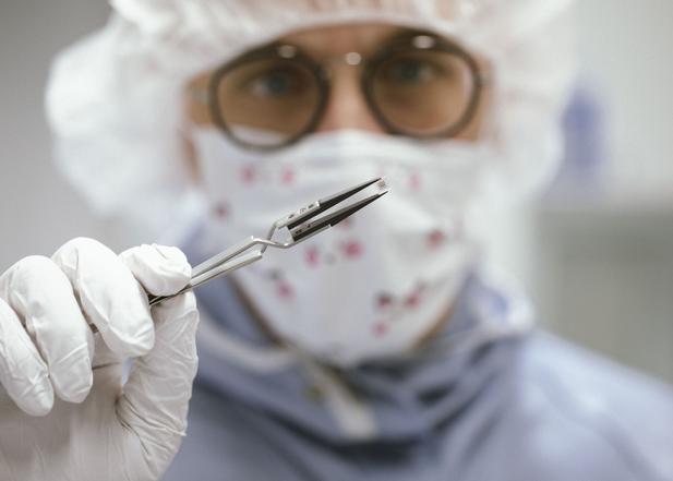 A laboratory employee holds a miniaturized medical implant with tweezers