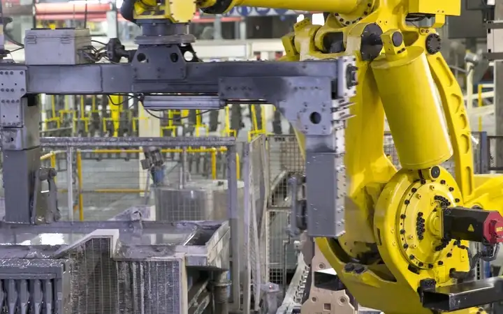 Yellow robot moves a metal part in a factory