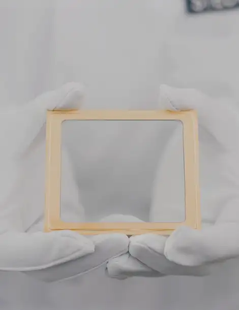 Hands with white gloves holding a MEMS window with golden frame