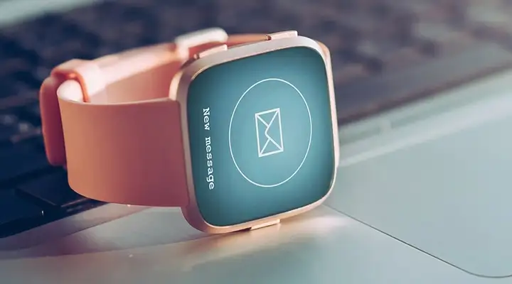 Smartwatch with an orange strap on top of a silver laptop compute