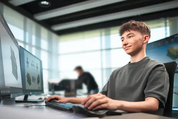 Eine Person arbeitet an einem Computer mit mehreren Monitoren und betrachtet technische 3D‑Modelle.