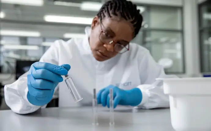 Woman in cleanroom clothing holding a large-volume prefillable glass syringe from SCHOTT Pharma.