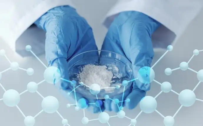 Close up of gloved hands holding a petri dish full of white glass powder