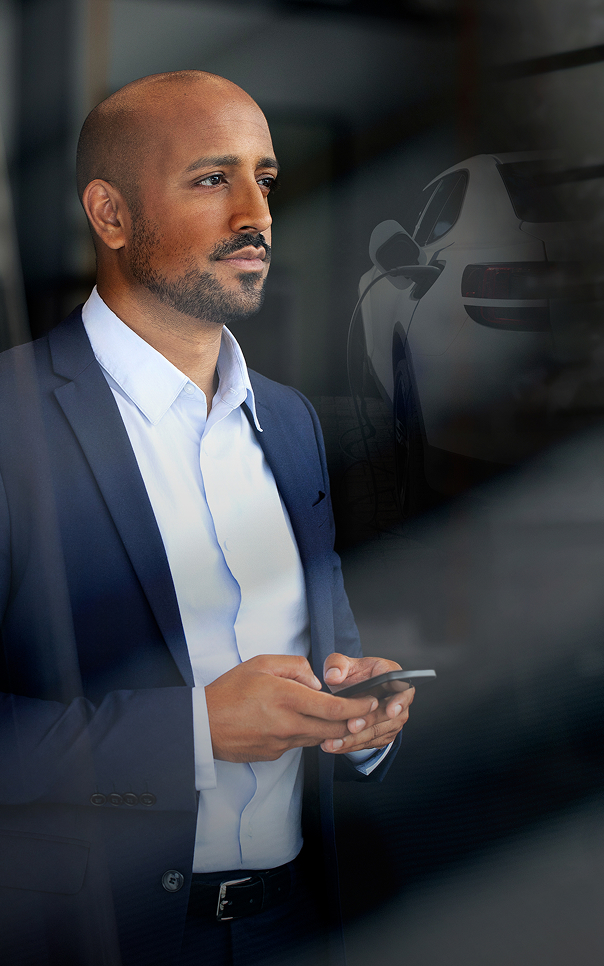 Eine Person in einem Business‑Anzug steht vor einem Schaufenster oder Glasbereich und hält ein Smartphone in den Händen.