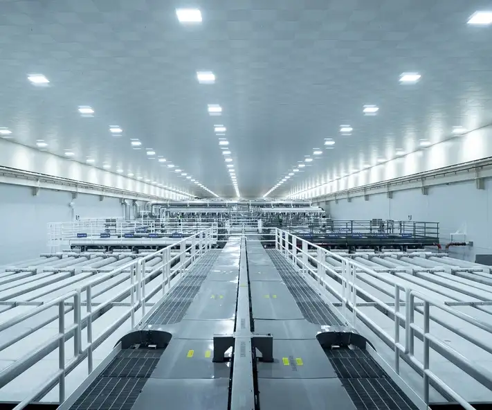 Une immense salle blanche avec de longs tuyaux et des passerelles qui s’étendent à perte de vue.