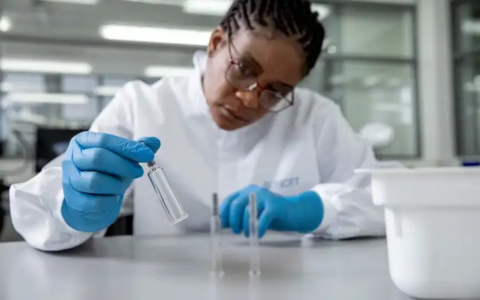Woman in cleanroom clothing holding a large-volume prefillable glass syringe from SCHOTT Pharma.