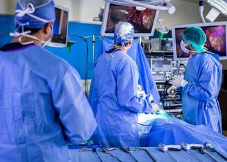 Doctors watch HD monitors while performing minimally invasive robotic surgery