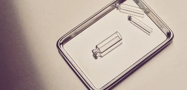 Three small clear glass vials on a reflective metal tray