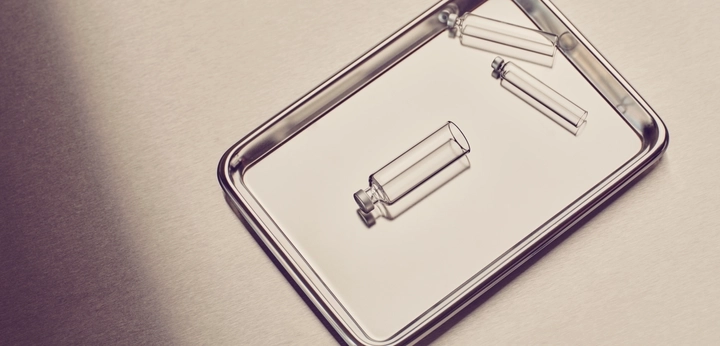 Three small clear glass vials on a reflective metal tray