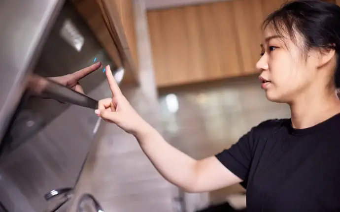 Person using a touch  interface on an extractor hood.  With wooden cabinets and tiled walls in the background.
