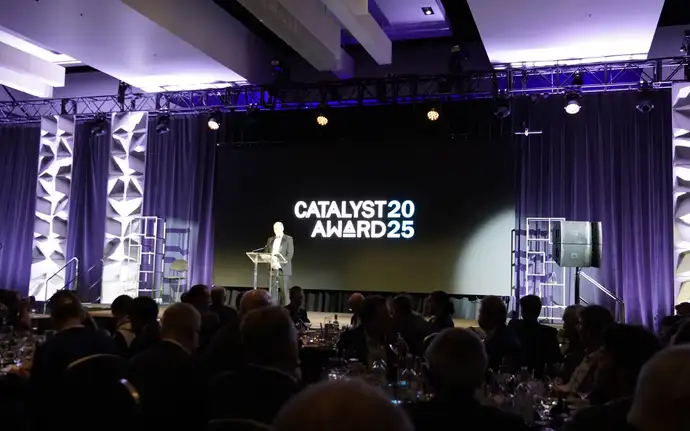 The presenter is standing on stage with people sitting down viewing him. 