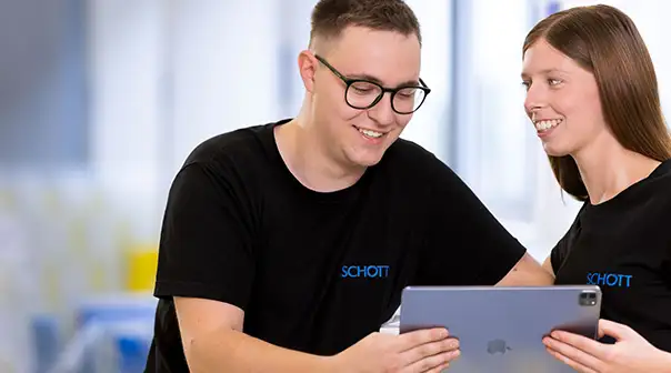 Zwei Personen in SCHOTT-T-Shirts schauen gemeinsam auf ein Tablet.