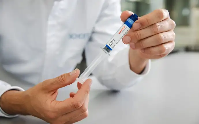 Man in white coat with SCHOTT logo holding a polymer syringe.