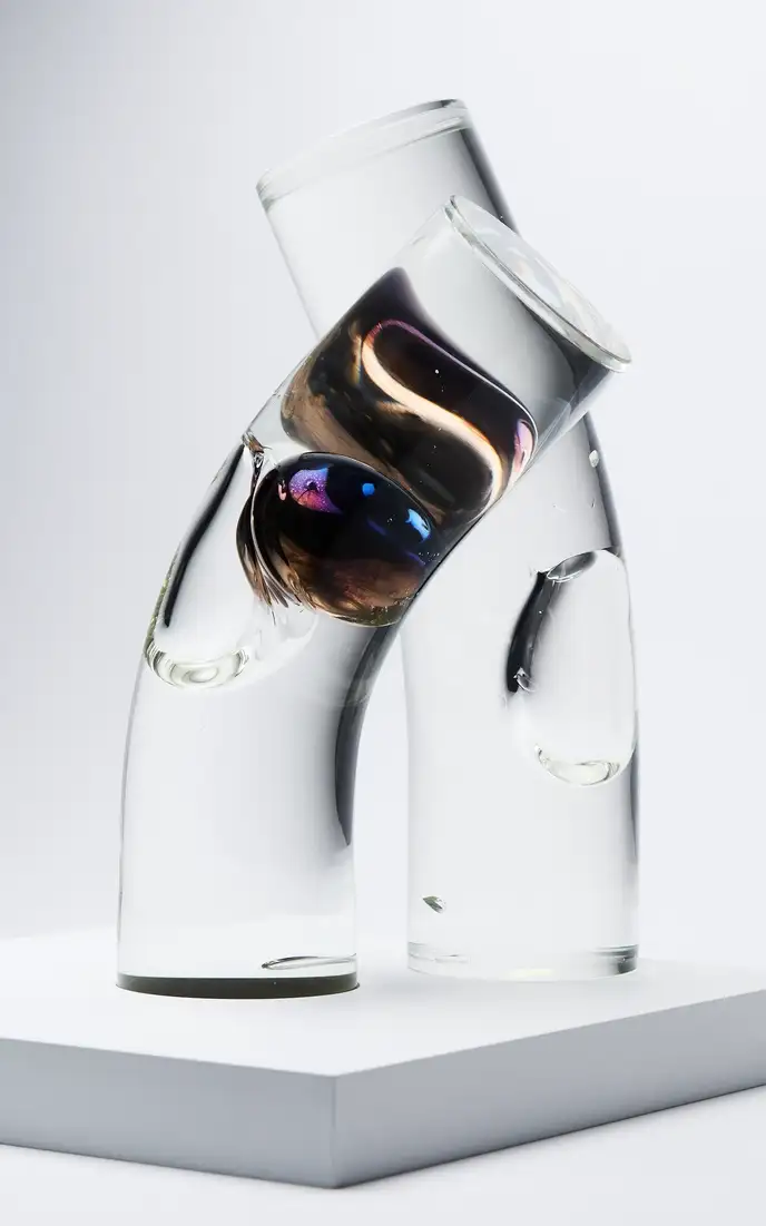 Abstract arrangement of three clear glass vessels balancing on a white pedestal, with dark iridescent reflections.