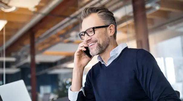 Man in glasses in business office on phone while working on laptop"