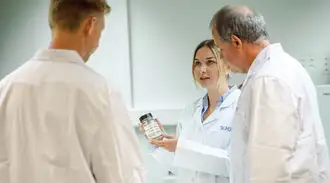 Nina Hoinkis talks to her colleagues, holding a glass bottle from the lab