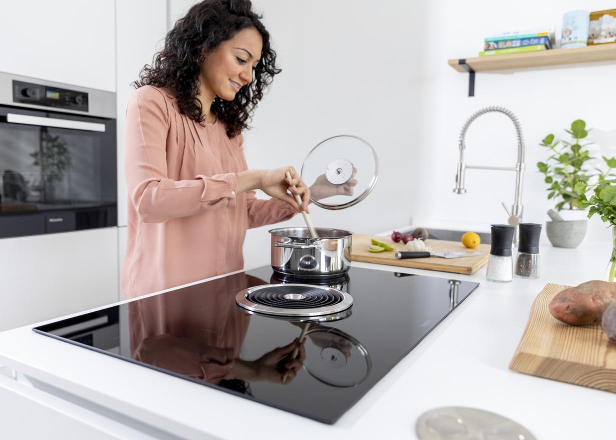 Woman in kitchen cooking food on a hob with CERAN® glass-ceramic cooktop