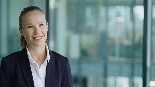Eine Person in Businesskleidung steht in einem modernen Bürogebäude und blickt nach vorn.