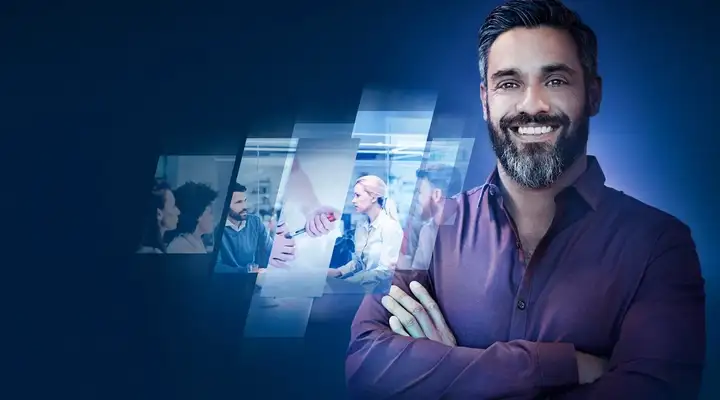 Bearded man with arms folded smiling in front of images of professionals in a meeting