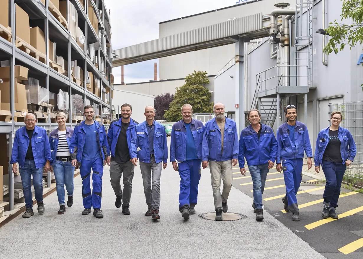  Michael Hahn and his colleagues walking side by side in their blue work gear on the SCHOTT premises in Mainz