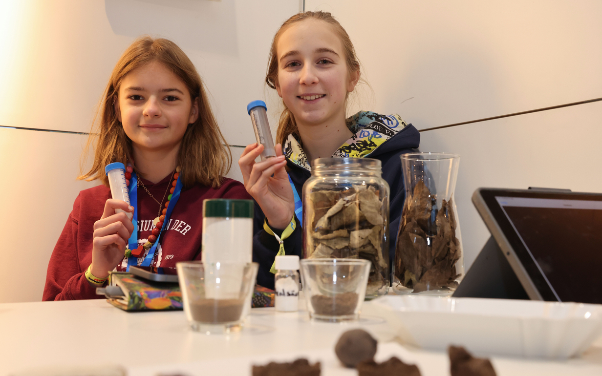 Marlene-Luise Schöttke und Valerie-Kristine Huber halten Bioplastikröhrchen in die Kamera. Im Vordergrund Gläser mit getrockneten Blättern.