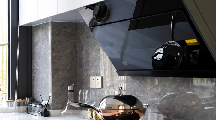 Modern kitchen with a black extractor hood made of glass, sleek white countertops, a gas glass hobtop, and various kitchen utensils near a large window.