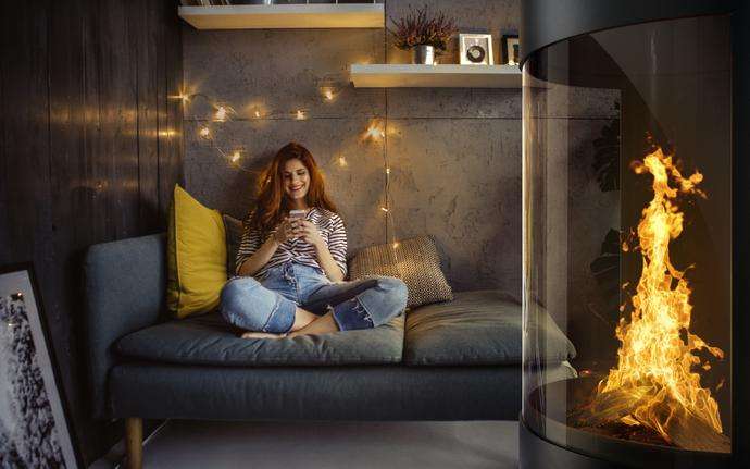 Woman sitting with her smartphone on a sofa beside a fireplace