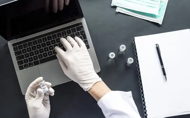 Person sitting in front of laptop with vial in hand